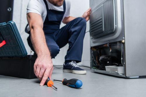 Technician repairing an open appliance with tools on the floor, working beside a detached panel