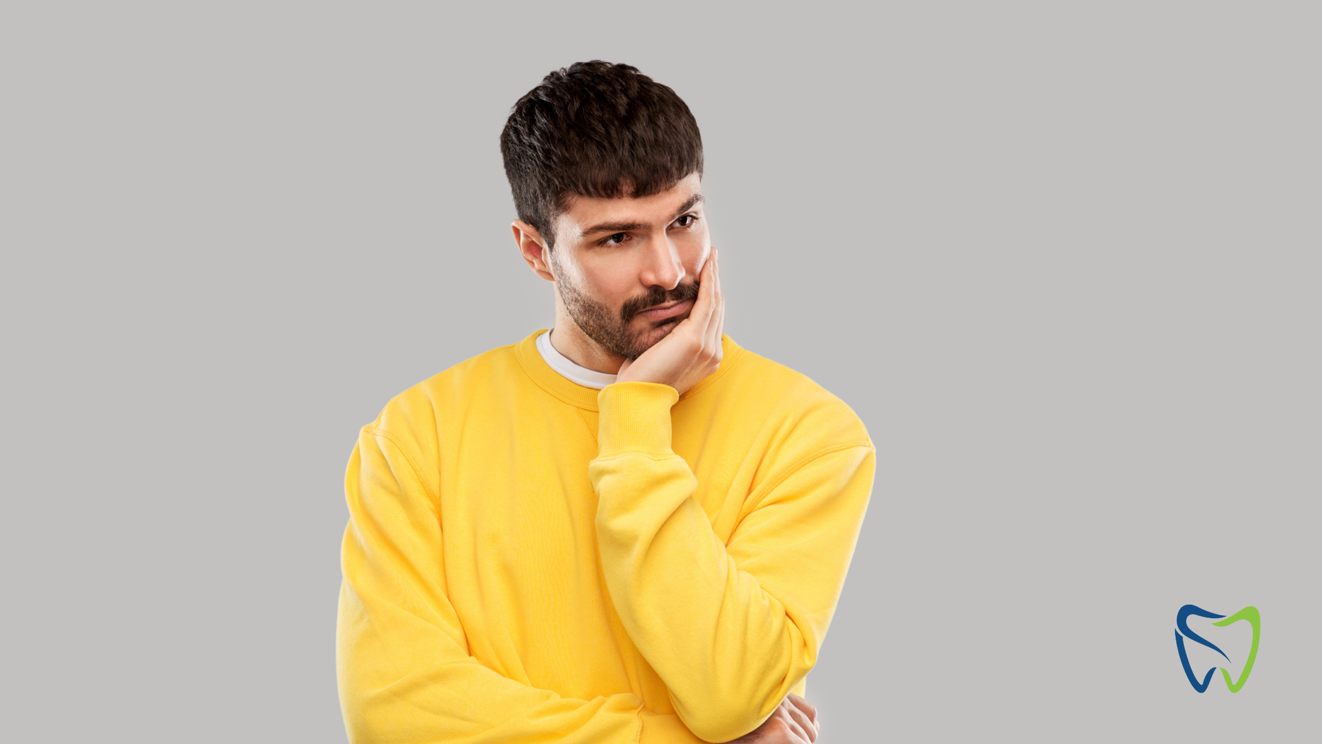 A man in a yellow sweater is holding his hand to his chin.