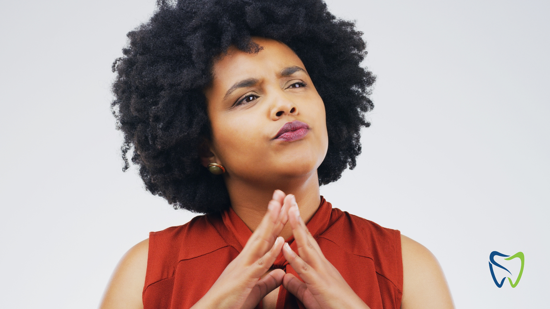 Woman with dark curly hair looking thoughtful, chin resting on clasped hands.