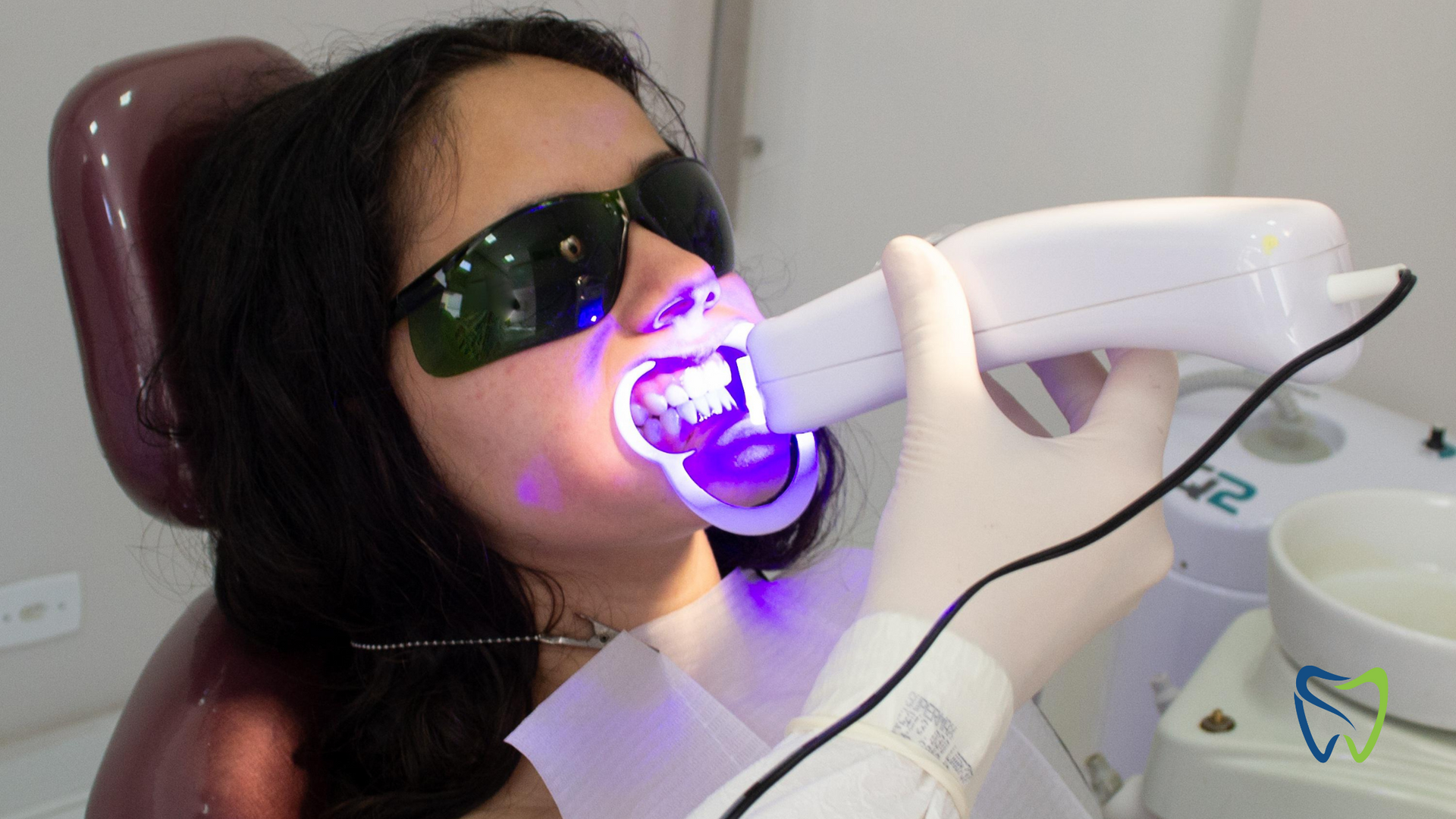 Person in sunglasses receiving purple light treatment on teeth from a dental device