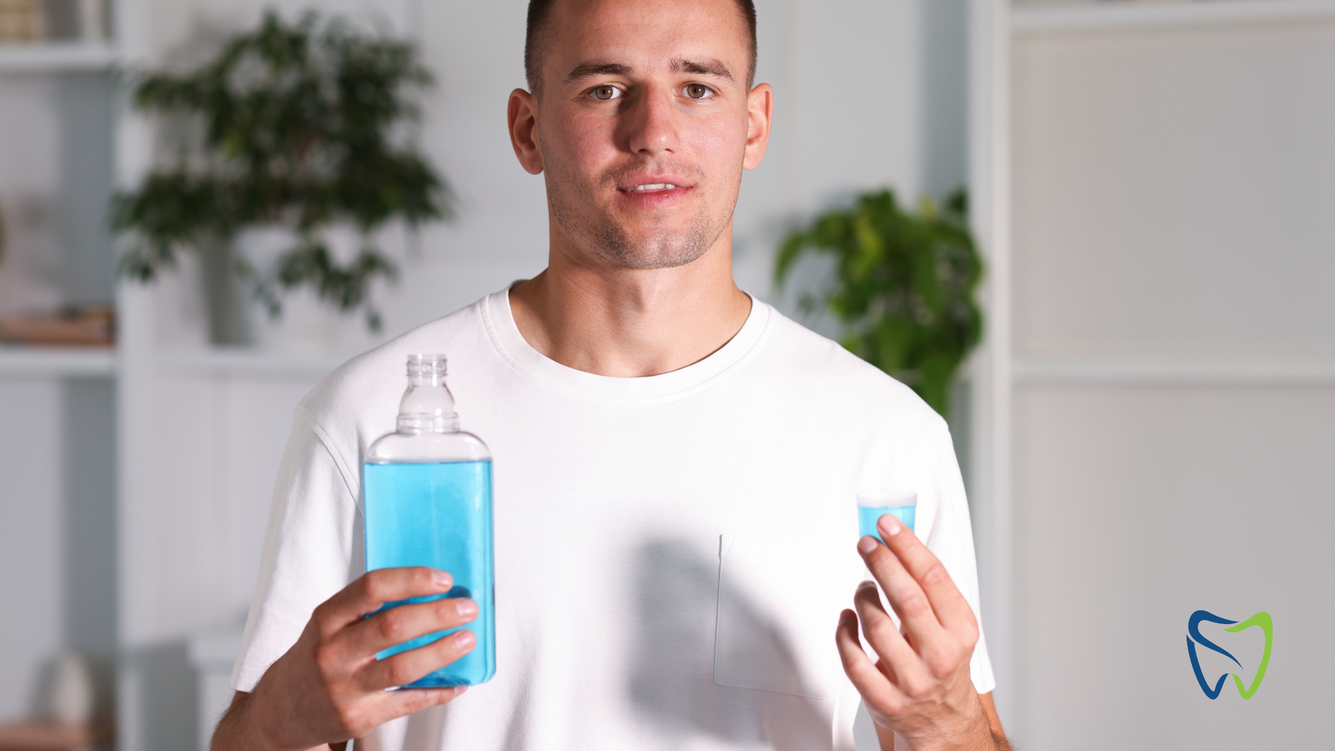 Man holding blue mouthwash and cup; in a bathroom.