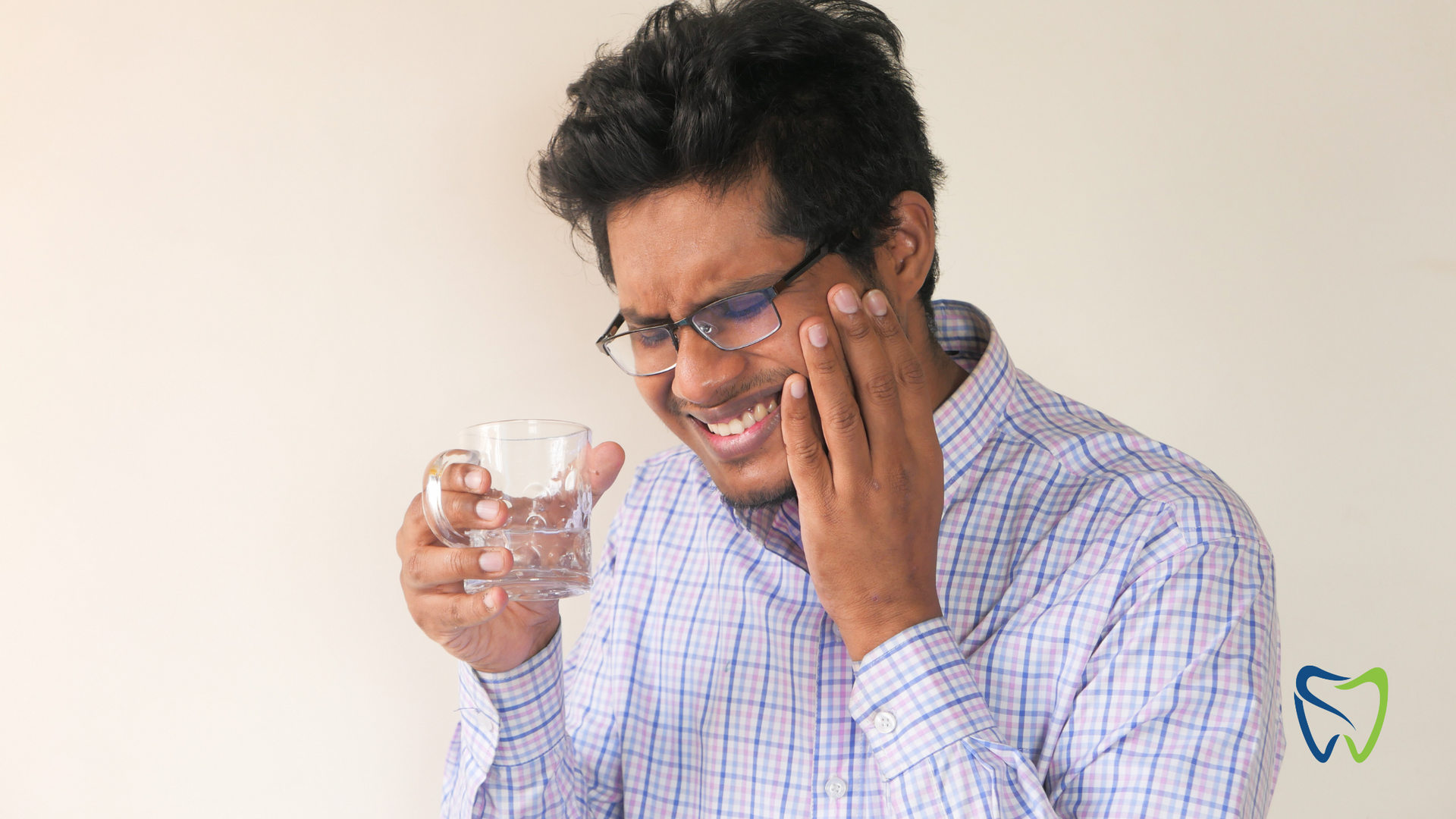 Man holding a glass of water and touching his cheek, grimacing in pain or discomfort.