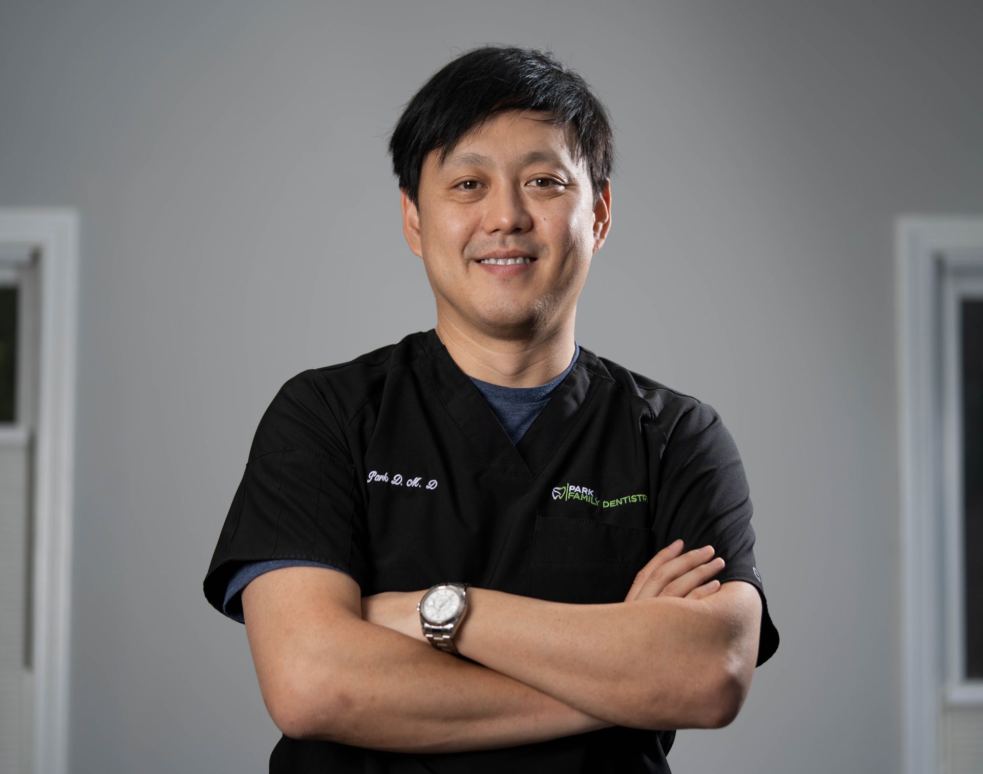 Smiling person in black shirt with arms crossed against a gray studio background