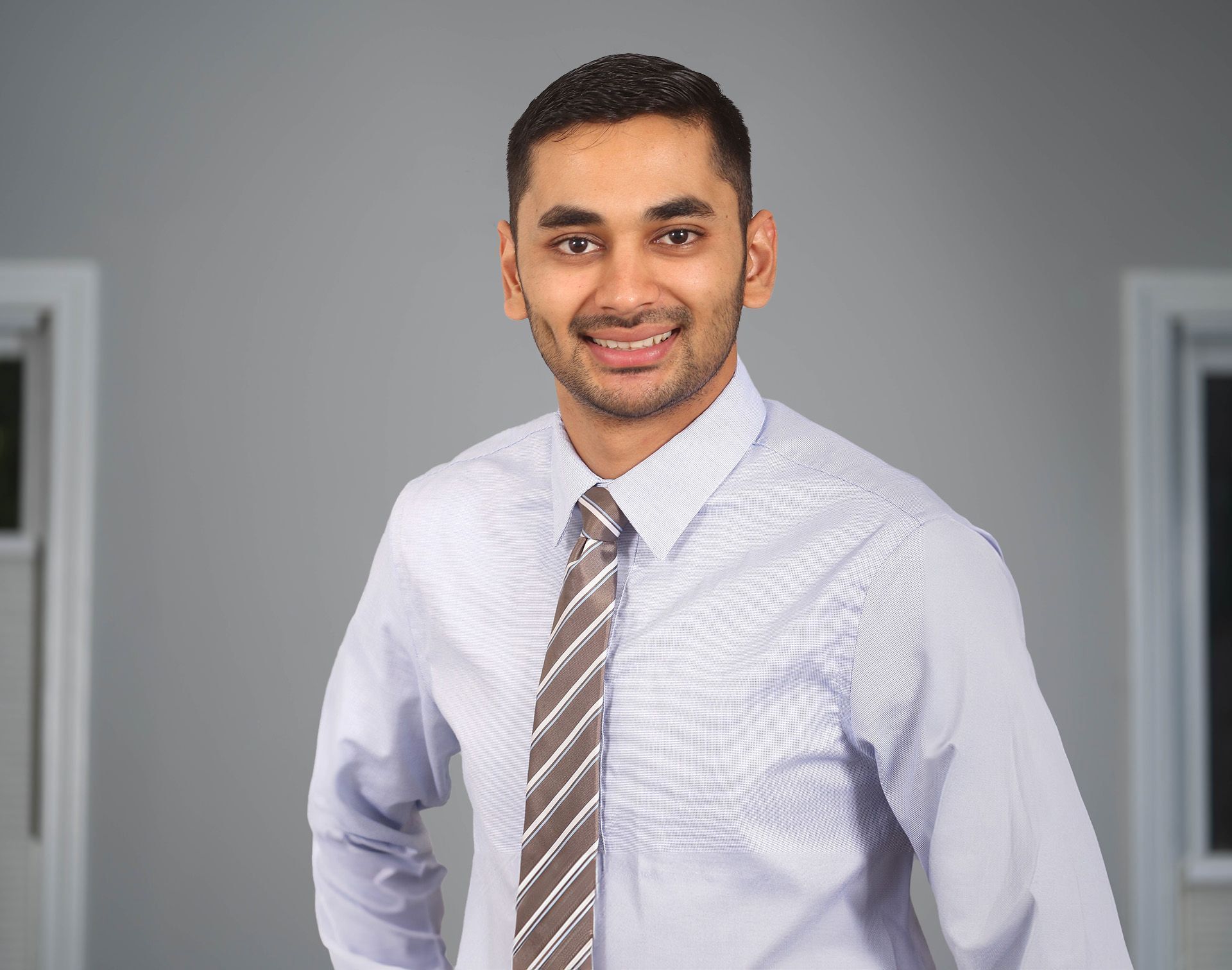 Man in a striped shirt and tie smiling in an office hallway