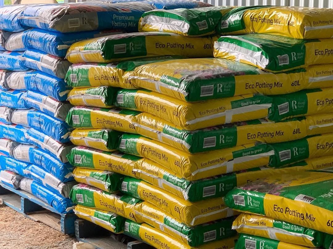 Stacked bags of fertilizer or animal feed in blue, green, and yellow packaging on pallets in a warehouse — Sunny Ridge Nursery in Fairy Bower, QLD