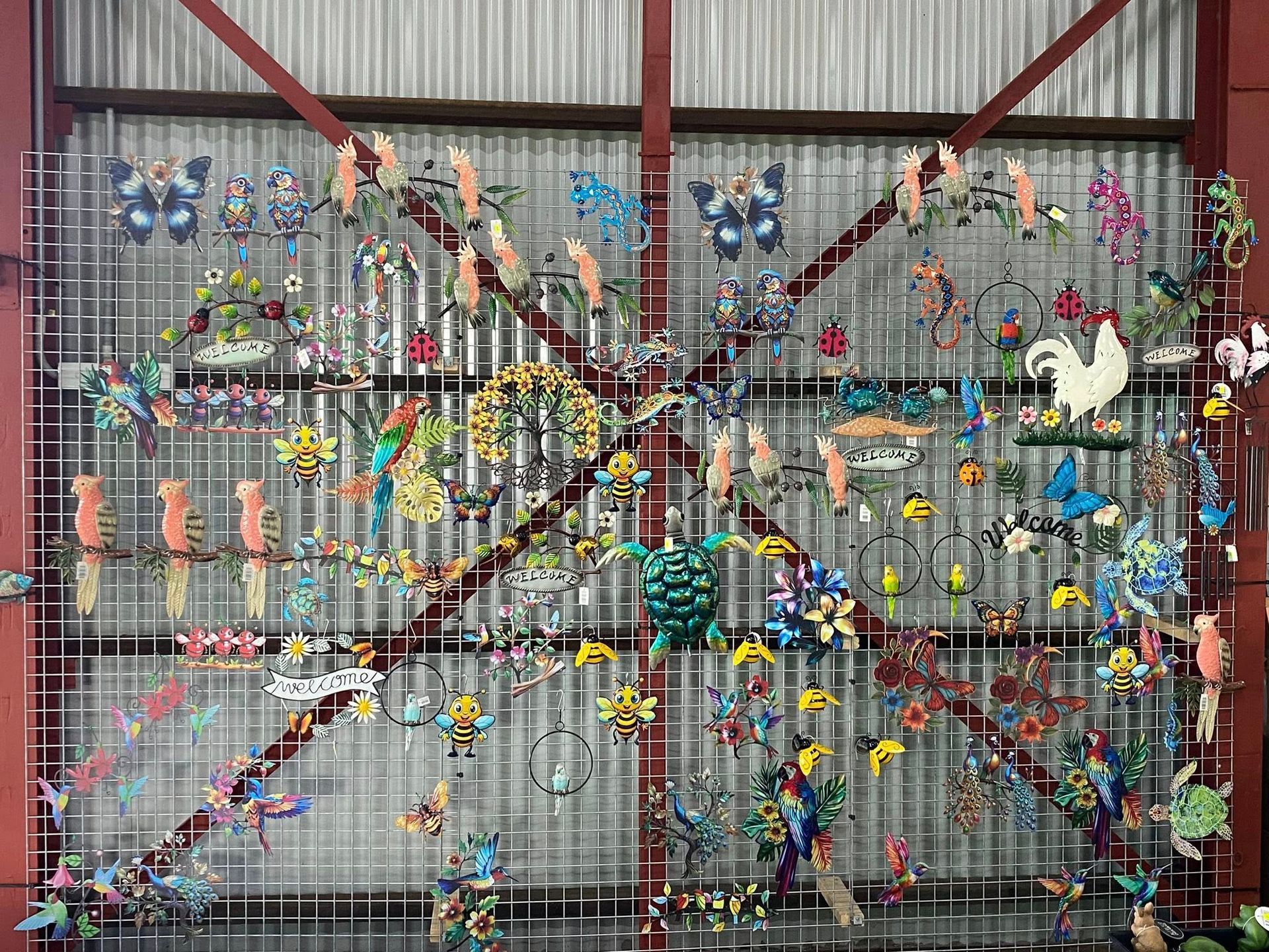 A grid display wall covered in colorful, decorative metal garden ornaments like butterflies, birds, and sea creatures.