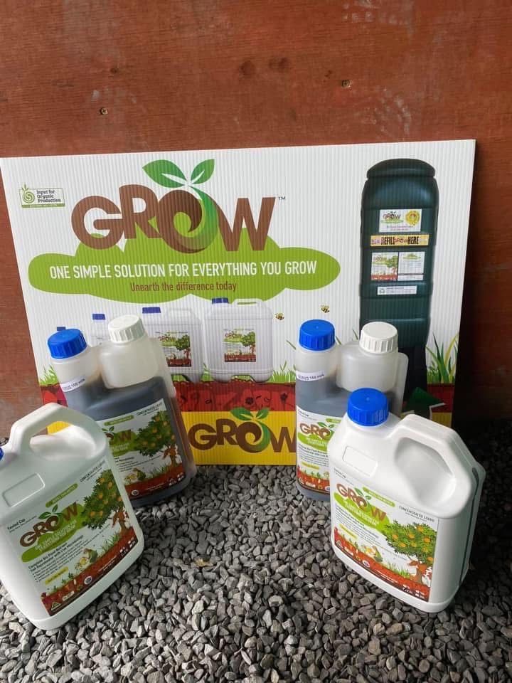 GROW fertilizer bottles and containers arranged on gravel with a branded product box behind them