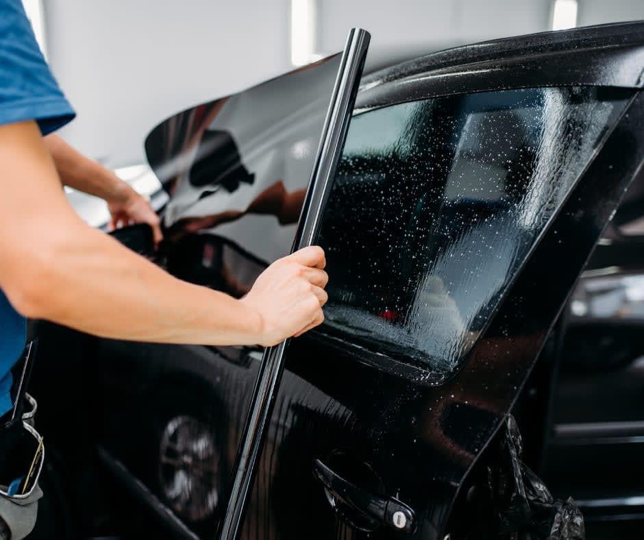 Person cleaning a black car window with a squeegee at a car wash
