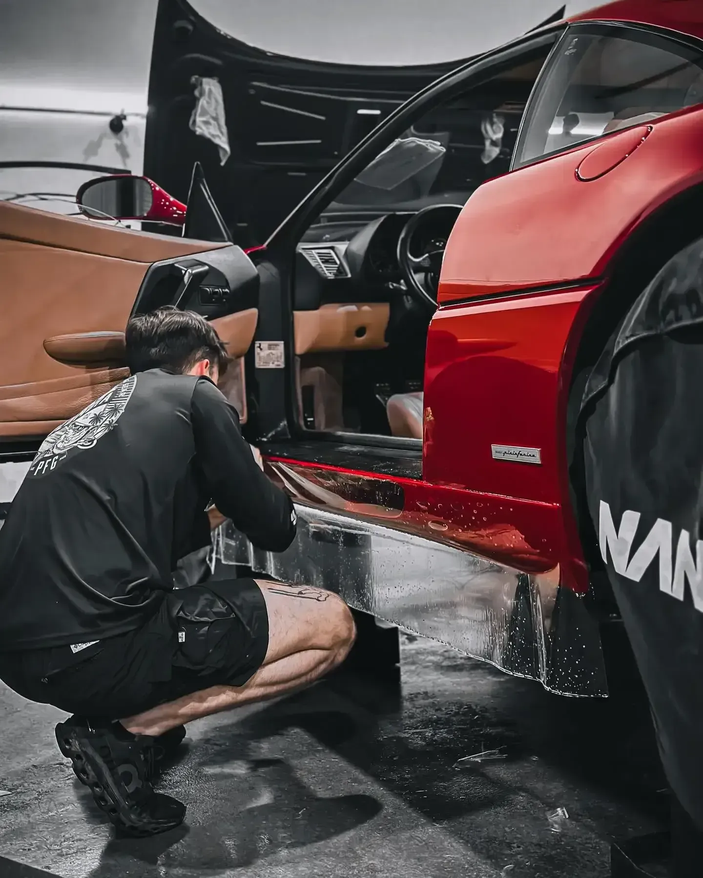 Mechanic crouches beside a red race car with its door open, working on the exposed interior.