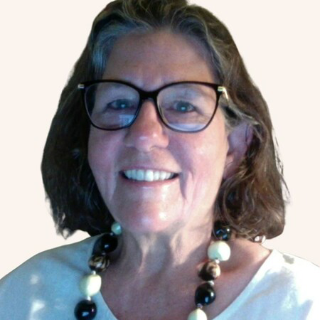 Woman with glasses smiles, wearing a beaded necklace and white top.