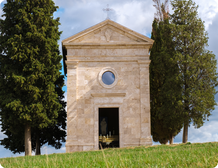 Chapel on a hilltop framed by cypress trees. Light stone exterior, circular window, open doorway.