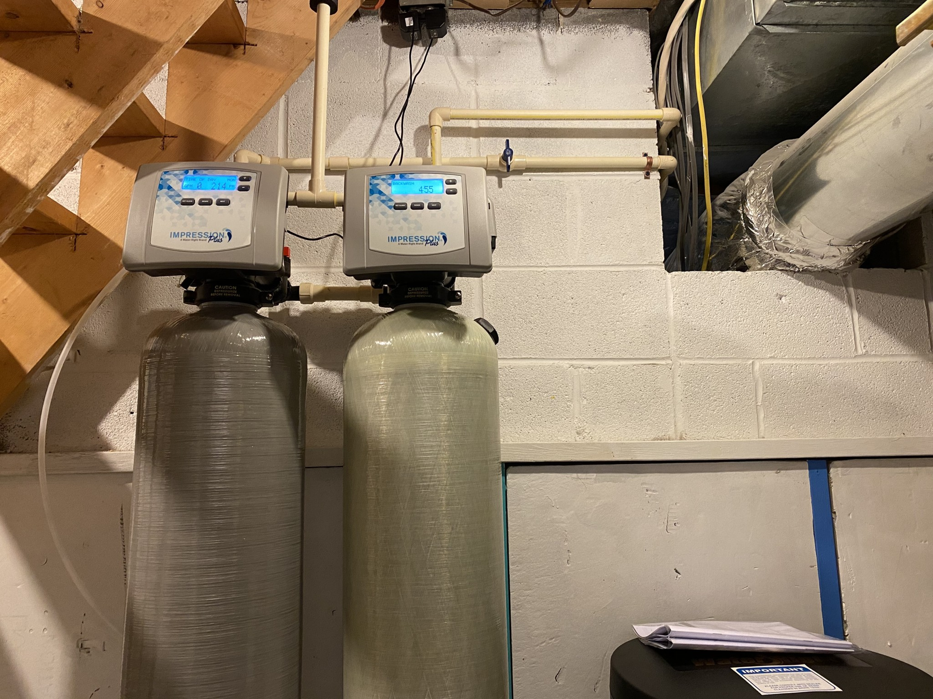 Two industrial water filtration tanks with digital control heads mounted against a white cinder block basement wall.