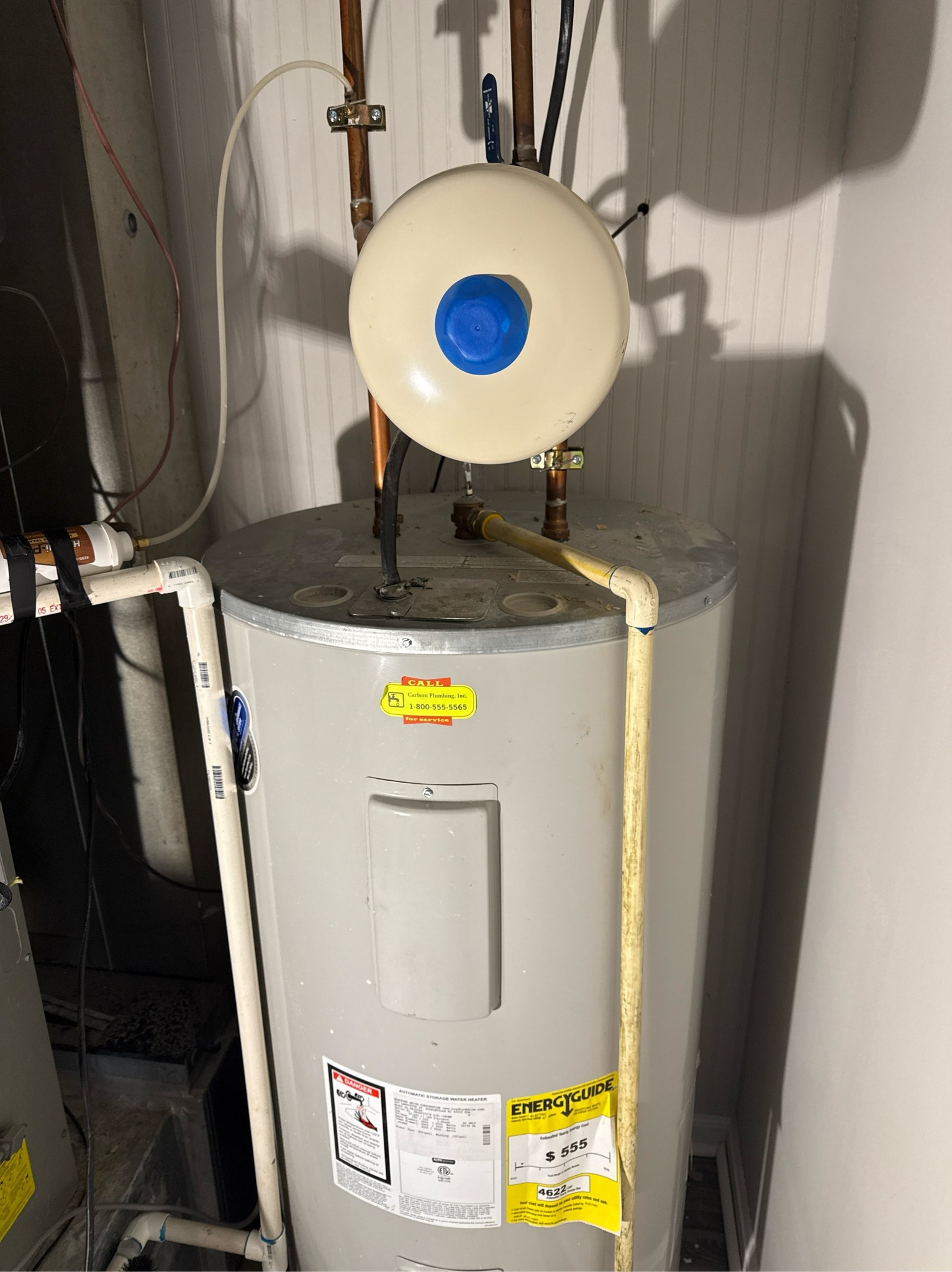 A water heater with a beige expansion tank mounted above it in a utility room setting.