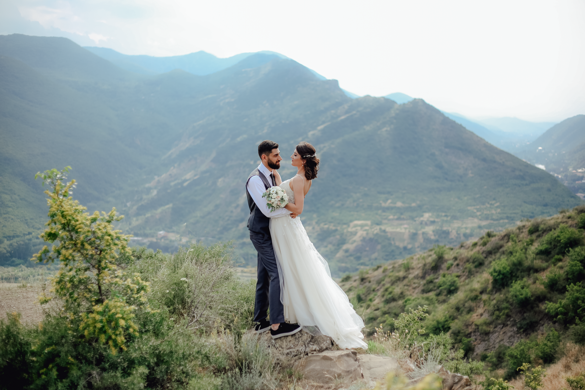 Bride and groom embracing on a mountain overlook with misty hills in the background