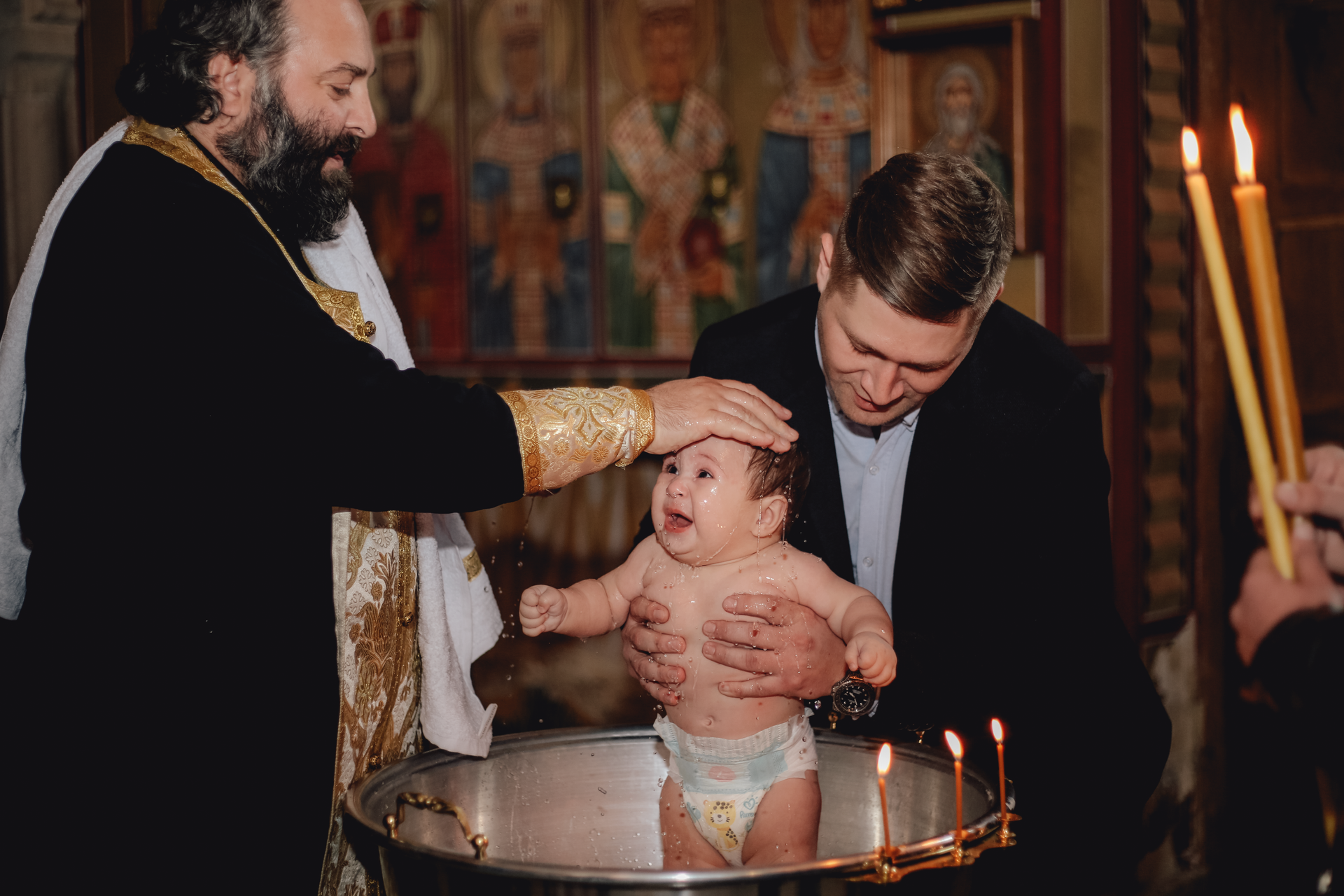 Priest pours water over a crying baby during a baptism ceremony in a church