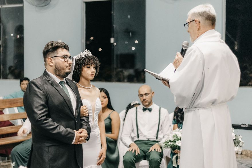 Wedding ceremony with couple facing an officiant in a white robe, guests seated behind them.