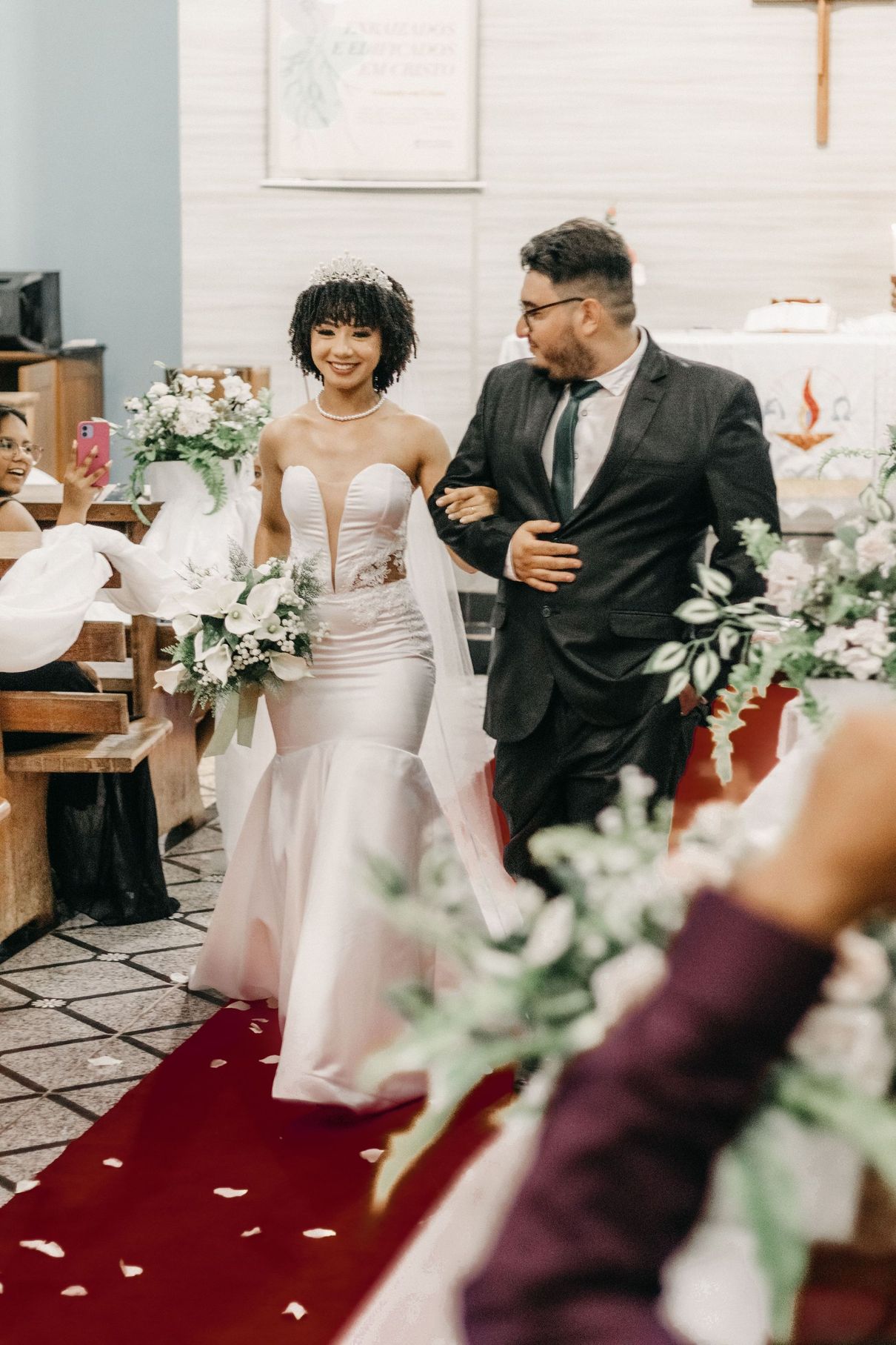 Bride and groom walking down the aisle in a church, with white flowers and red carpet.