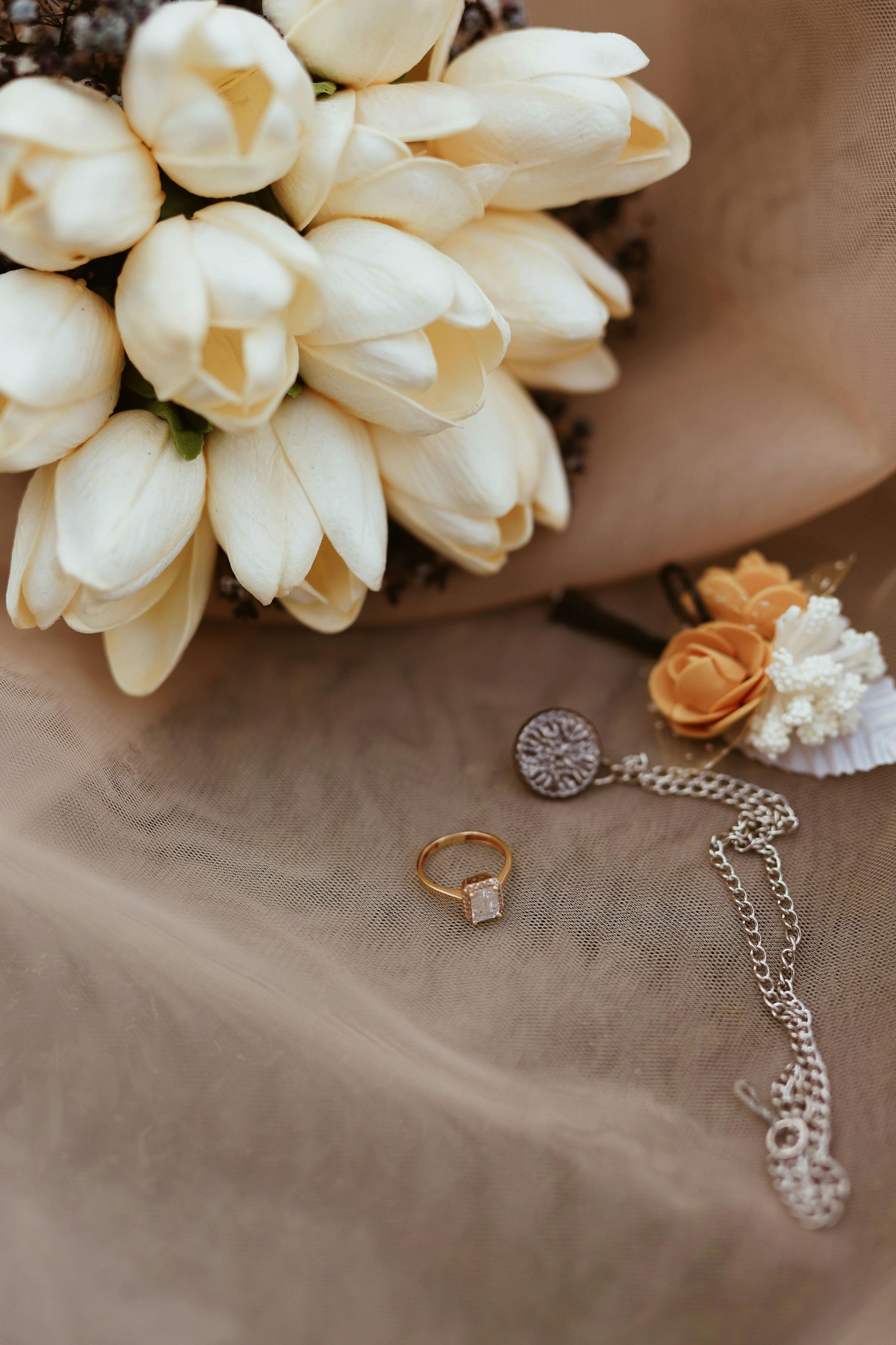 White flower bouquet with beige lace fabric and a delicate silver necklace on a tan background