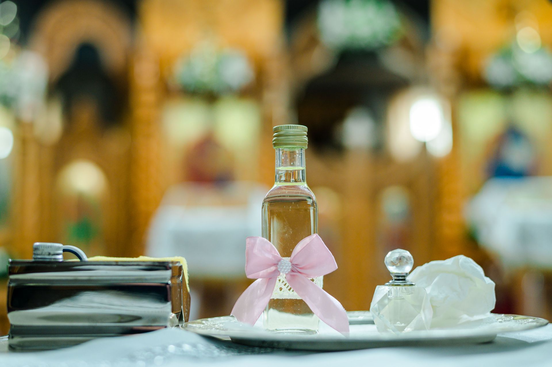 Small perfume bottle with a pink bow beside a glass and folded napkins on a table in a blurred café setting