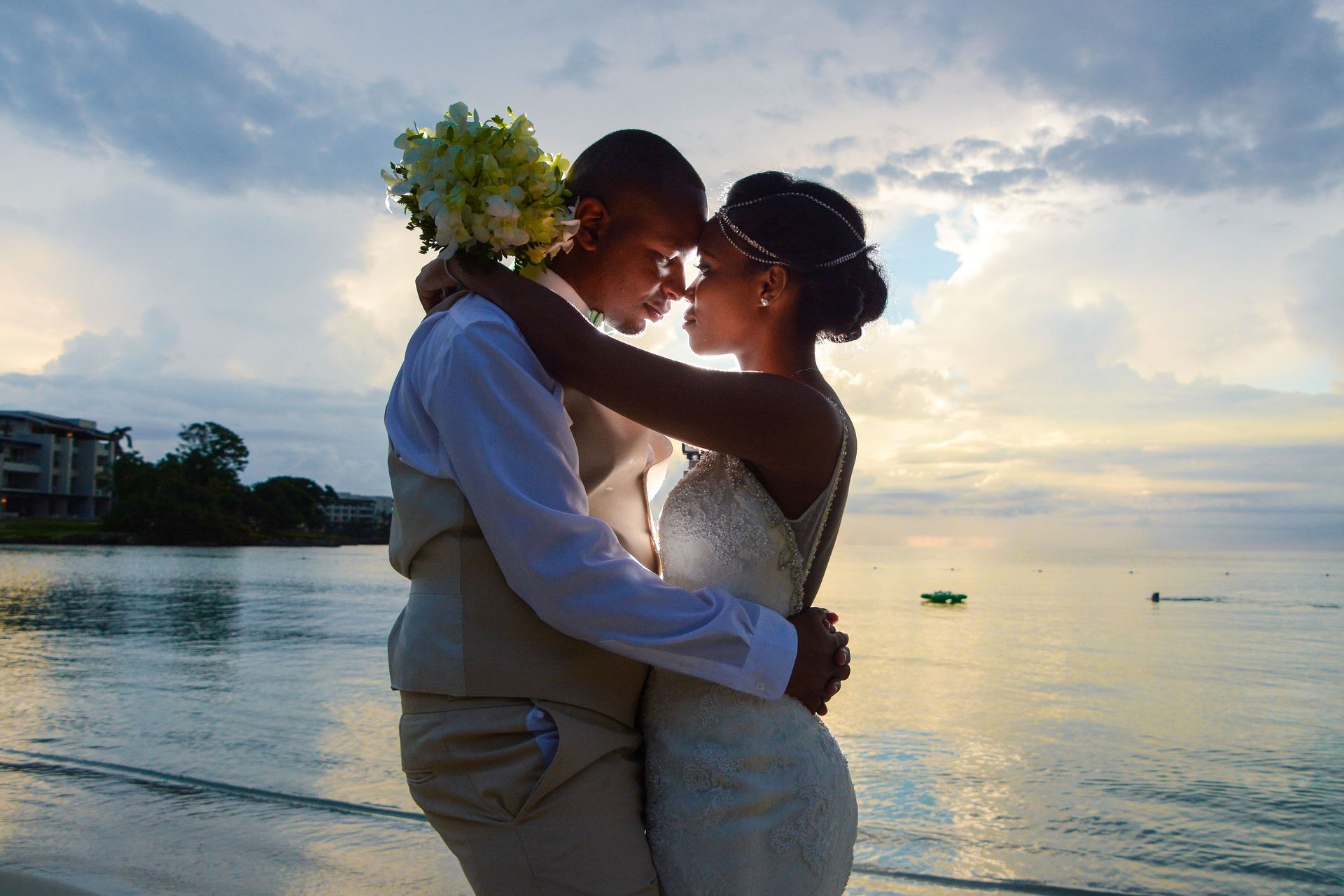 Couple embracing and kissing at sunset by the water, with warm golden light reflecting on the calm sea.