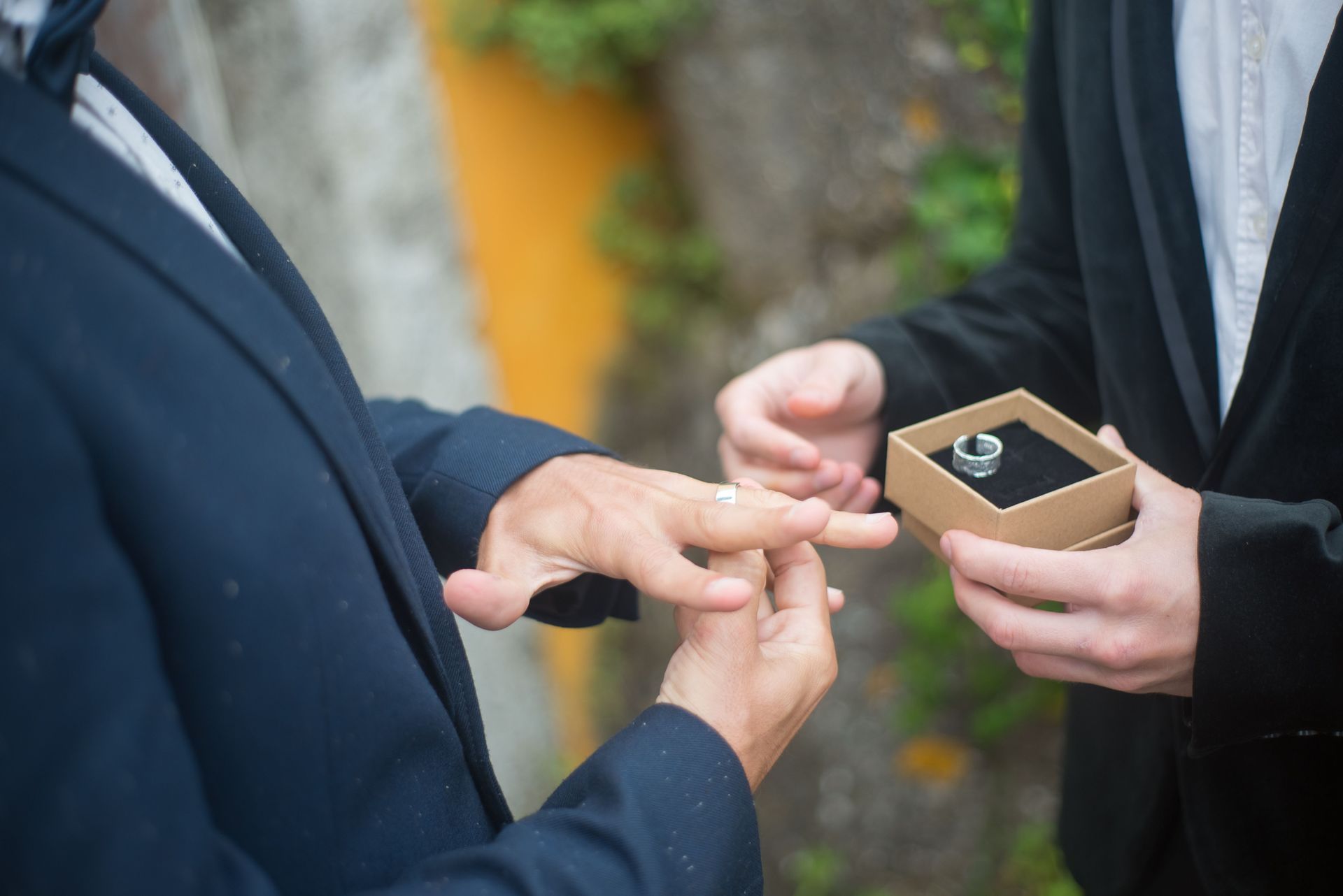 Hands exchanging a ring in a small box during an outdoor ceremony