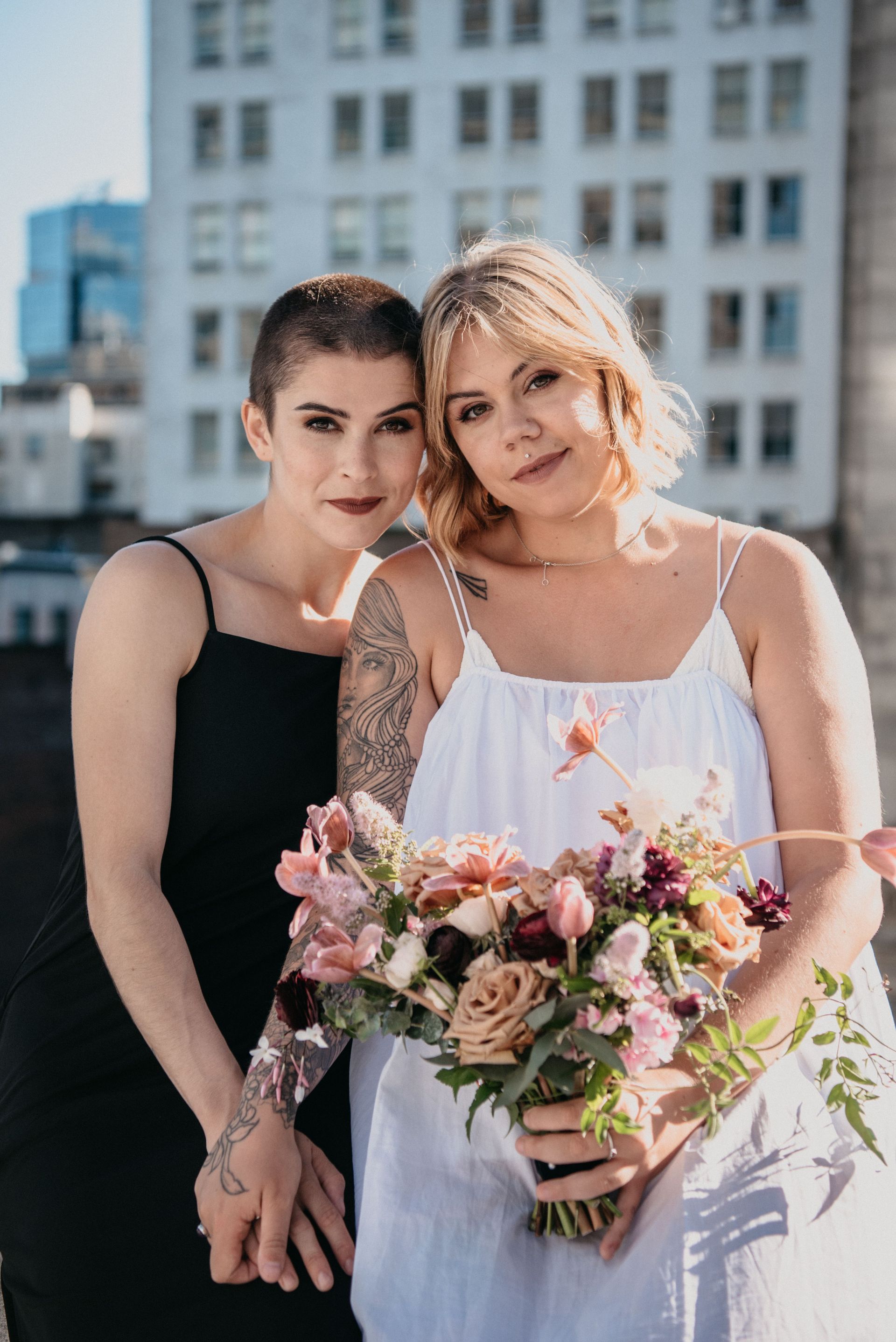 Two women at an outdoor ceremony, one holding a pink flower bouquet