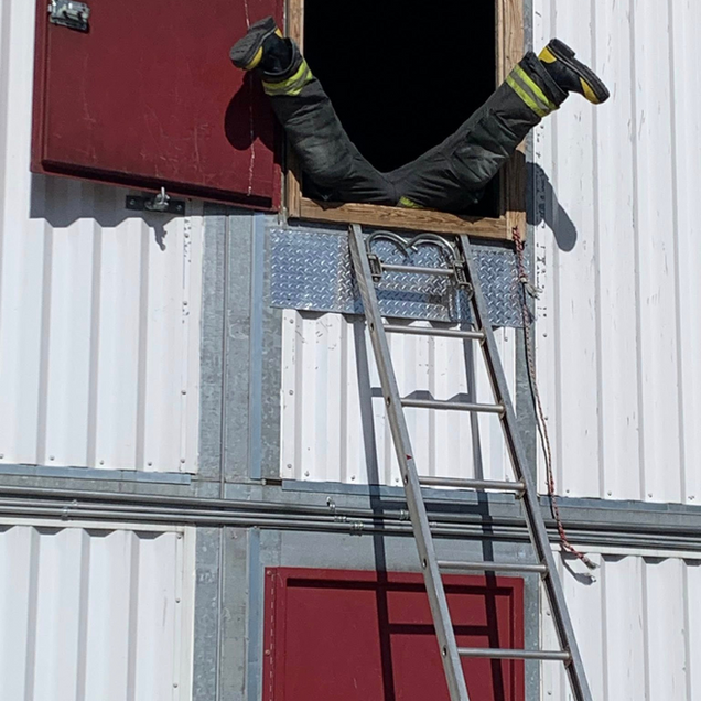 Worker’s legs protrude from a red window in a metal building while standing on a ladder