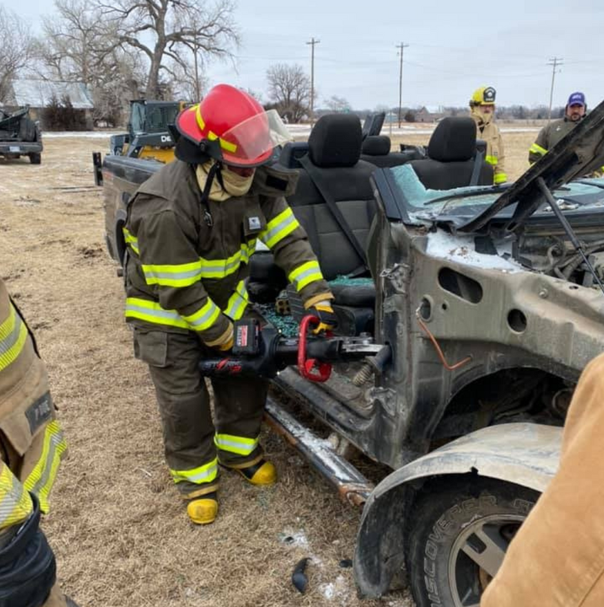 Firefighter using hydraulic rescue tool to cut car door in a training exercise.