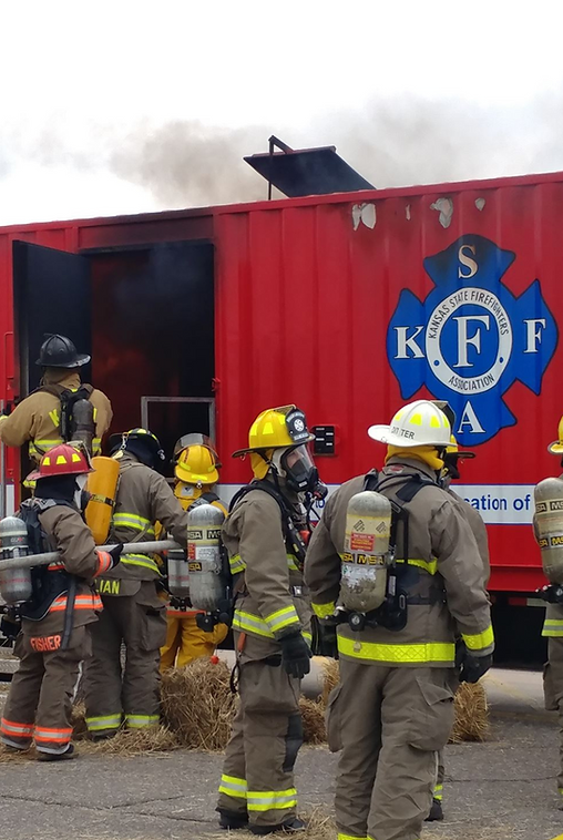 Firefighters gathered beside a red emergency vehicle with smoke rising from the top.