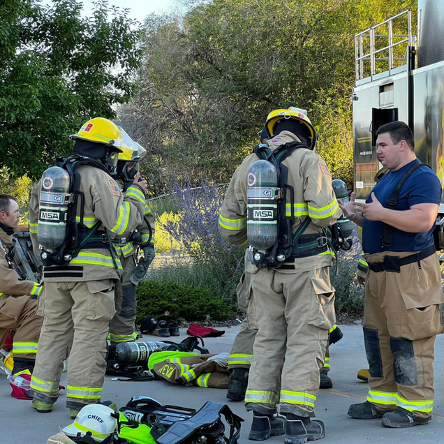 Firefighters in tan gear gather around a person on the ground during an emergency response.
