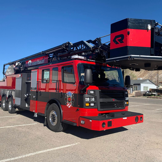 Red fire truck with extended ladder parked on a sunny lot, side view