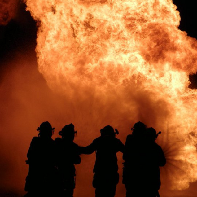 Firefighters silhouetted against a massive orange blaze at night