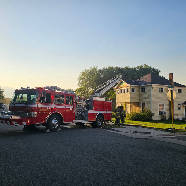 Fire truck and firefighters beside a yellow house with a ladder extended after a street-side emergency