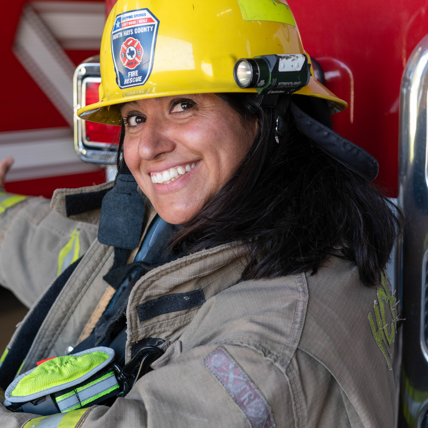 Smiling firefighter in a yellow helmet seated inside a fire truck, holding a radio.