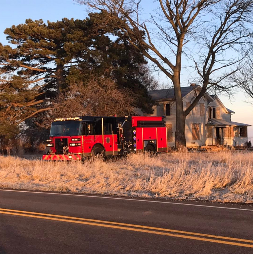 Red fire truck parked in tall grass beside a rural house at sunset