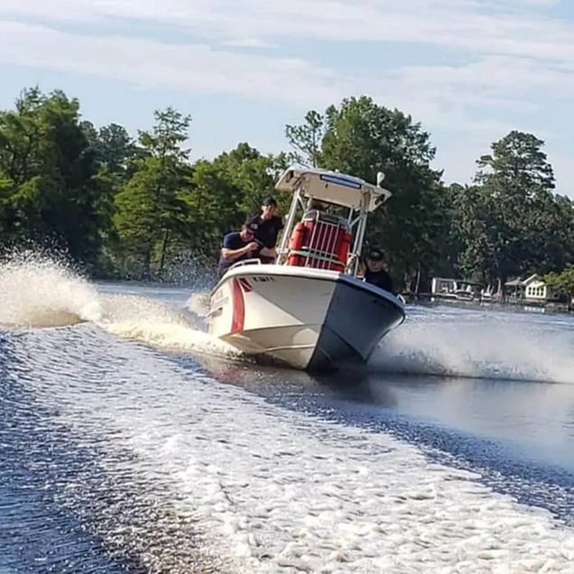 White speedboat racing across a lake, spraying water, with trees along the shore.