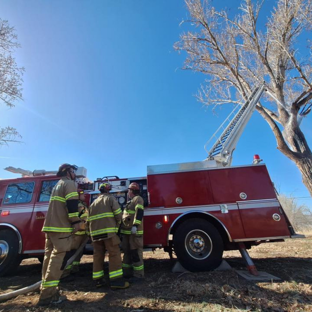 Firefighters beside a red fire truck with extended ladder, under a clear blue sky.