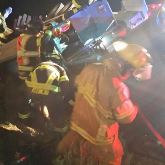 Firefighters in reflective gear working at night beside a damaged vehicle.