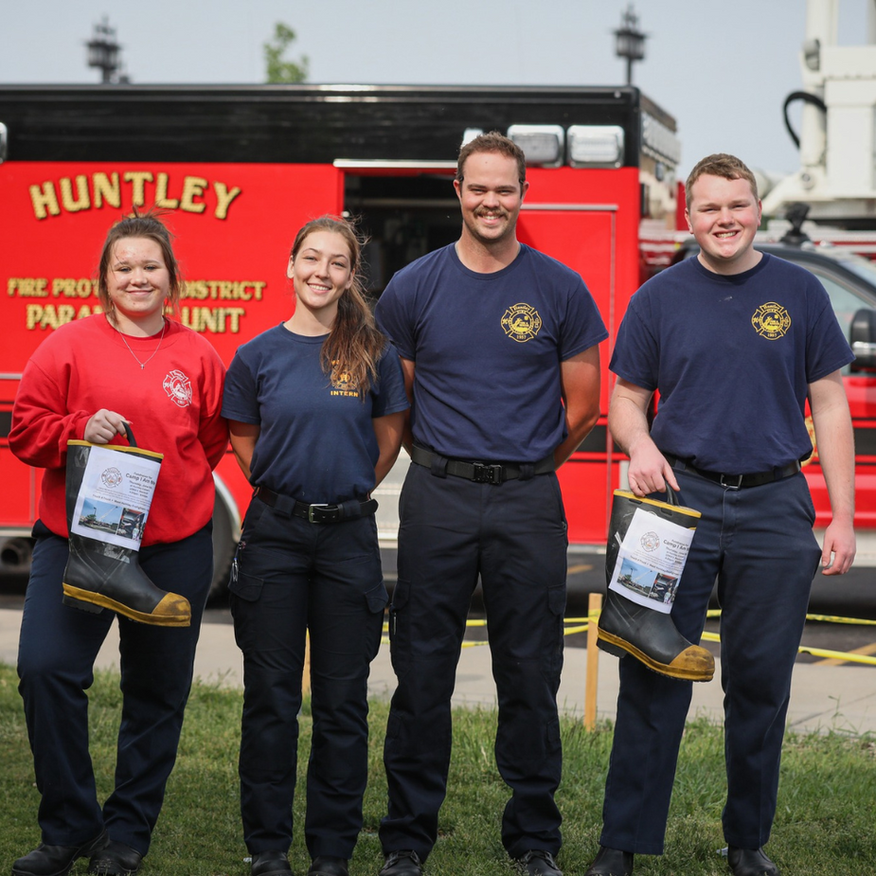 Four firefighters posing with boots in front of a red fire truck