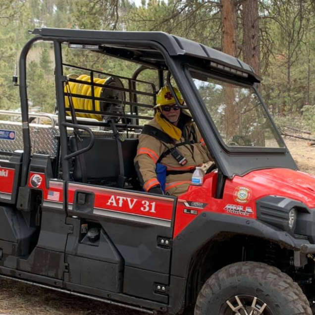 Utility ATV with a helmeted driver in an orange jacket on a wooded trail