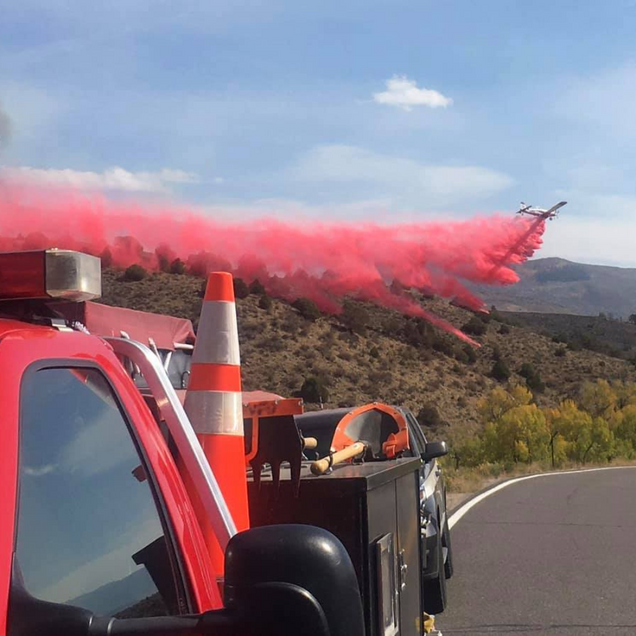 Fire truck on a road releasing bright pink smoke over a hillside under a blue sky