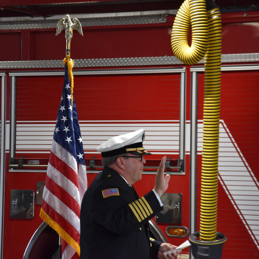 Firefighter saluting beside an American flag in front of a red fire truck.