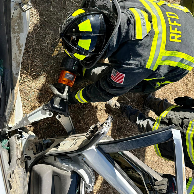 Firefighter using hydraulic cutters to extricate a person from a crushed car wreck.