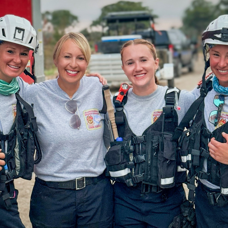 Four smiling team members in safety gear standing outdoors with a truck in the background