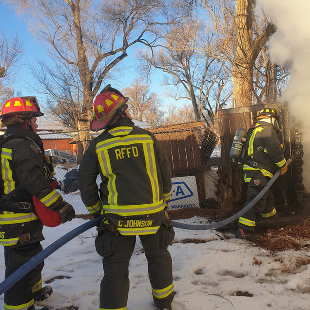 Firefighters in reflective gear work at a snowy house fire, spraying water near smoke and flames.