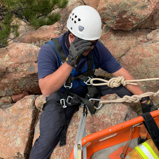 Climber in a white helmet rappels beside a rocky cliff, holding the rope on an orange harness system