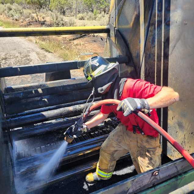 Firefighter spraying water inside a burned vehicle cabin with a hose