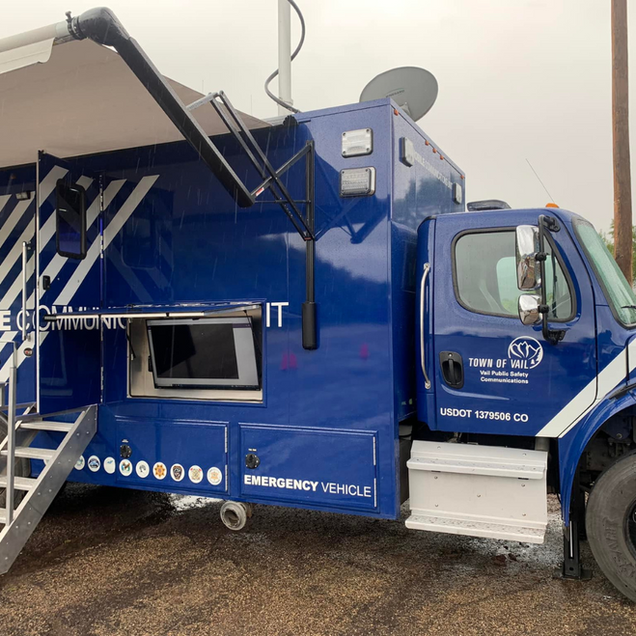 Blue emergency vehicle with ladder and open side hatch, parked outdoors.