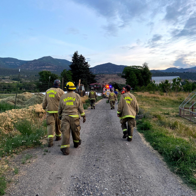 Firefighters in tan gear walking down a gravel road toward a wildfire response scene at dusk
