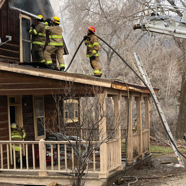 Firefighters on a house roof battling a blaze with a ladder truck nearby